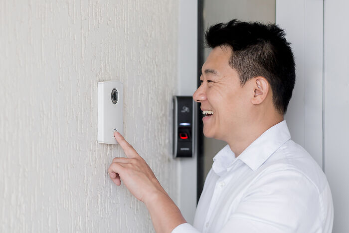 Man smiling while pressing a doorbell, wearing a white shirt, highlighting a commonly avoided item.