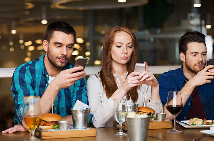 Young people using phones at a table, highlighting a social moment possibly pointing to Boomer insights on technology use.