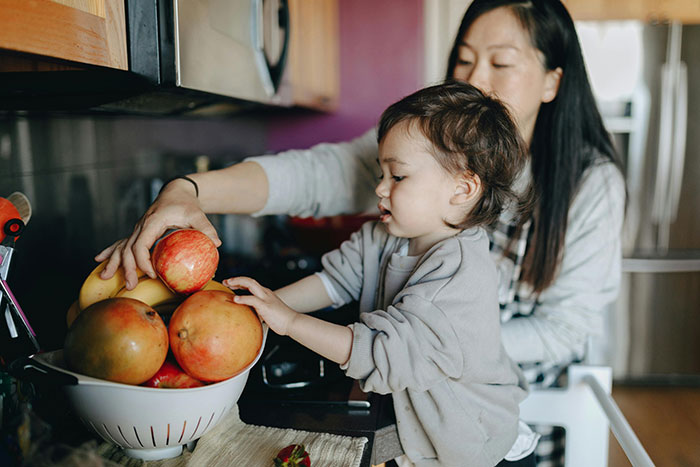 A mother and child reaching for fresh fruit in a kitchen, highlighting family values mothers appreciate about older generations.