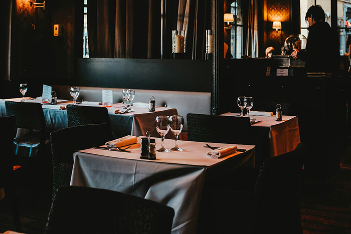 Empty restaurant with set tables, dim lighting, and a server at the counter.