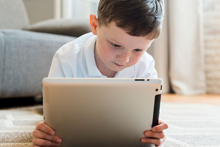 Young boy focused on a tablet while lying on a carpet, illustrating technology engagement.