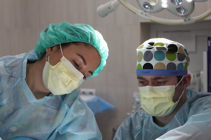 Two doctors in surgical scrubs and masks focused on a procedure, illustrating unfair treatment from doctors toward women.