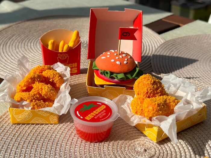 Toy food set with fake fries, a burger, chicken, and ketchup on a textured mat. Weird and creepy house finds theme.