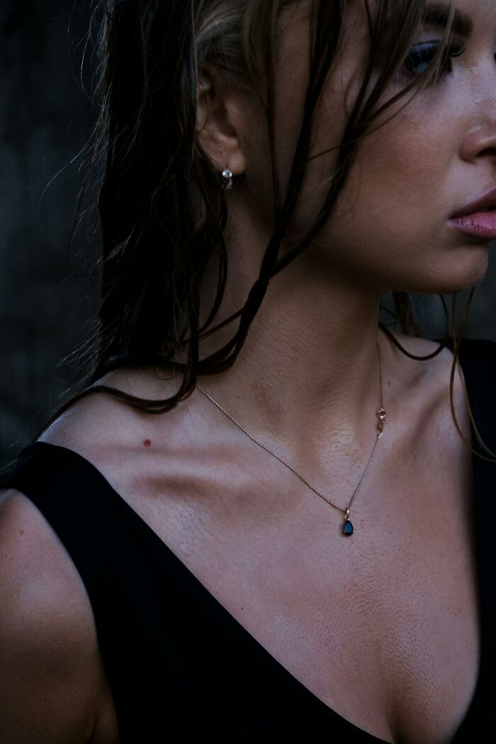 Close-up of a woman's neck and shoulders in a black top, wearing a delicate necklace.