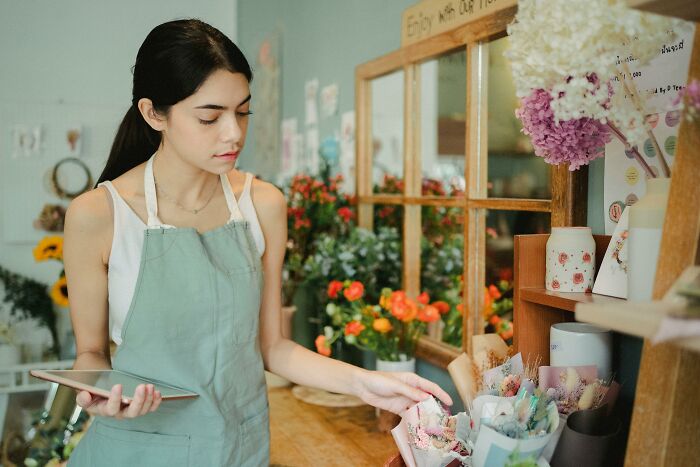 A florist holding a tablet, confidently arranging flowers in a shop, surrounded by vibrant blooms.