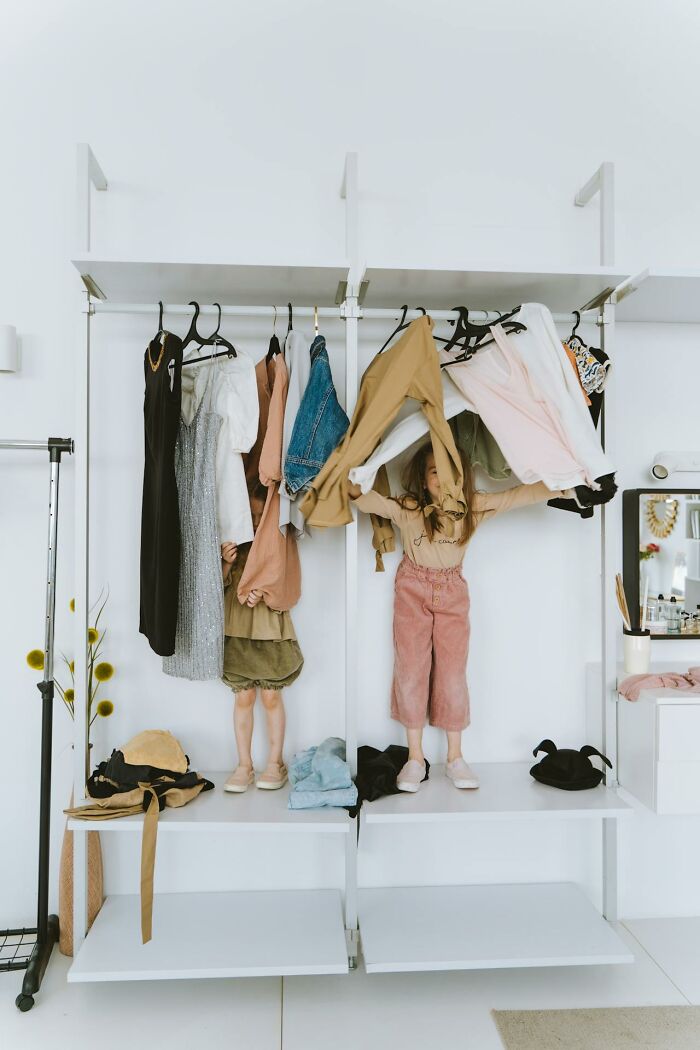 Child playing in a closet, surrounded by hanging clothes, illustrating mom sanity hacks.