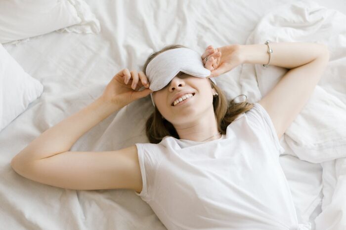 Smiling woman relaxing in bed with sleep mask.