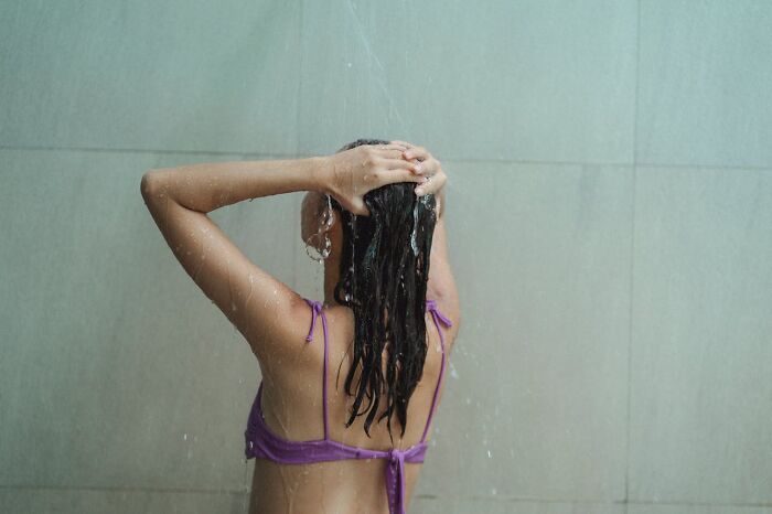 Person showering, emphasizing hygiene tips, wearing a purple top, running water rinsing hair in a bathroom setting.
