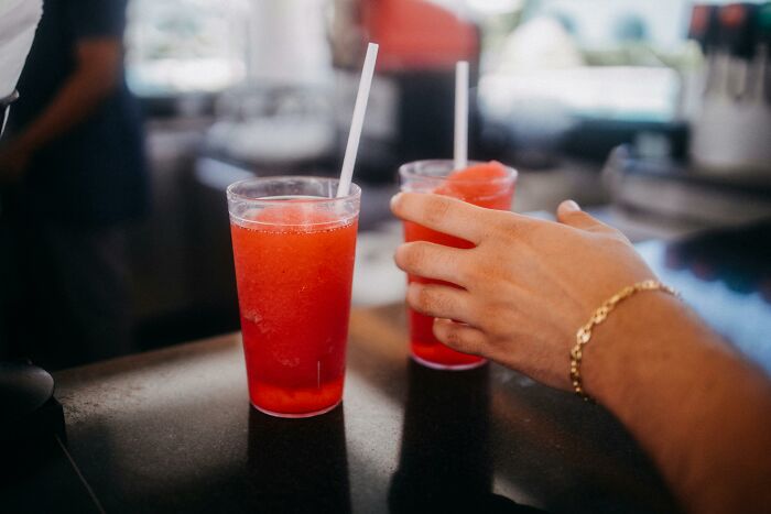 A hand reaching for red slush drink in a plastic cup on a counter, capturing a brief intrusive thought moment.