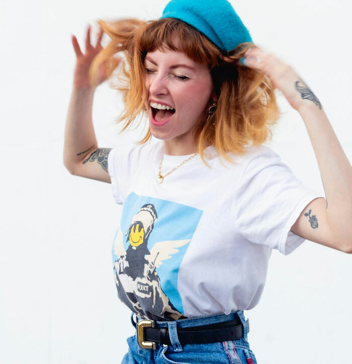 Woman expressing joy, wearing a graphic tee and blue hat, embodying unhinged mom sanity hacks.