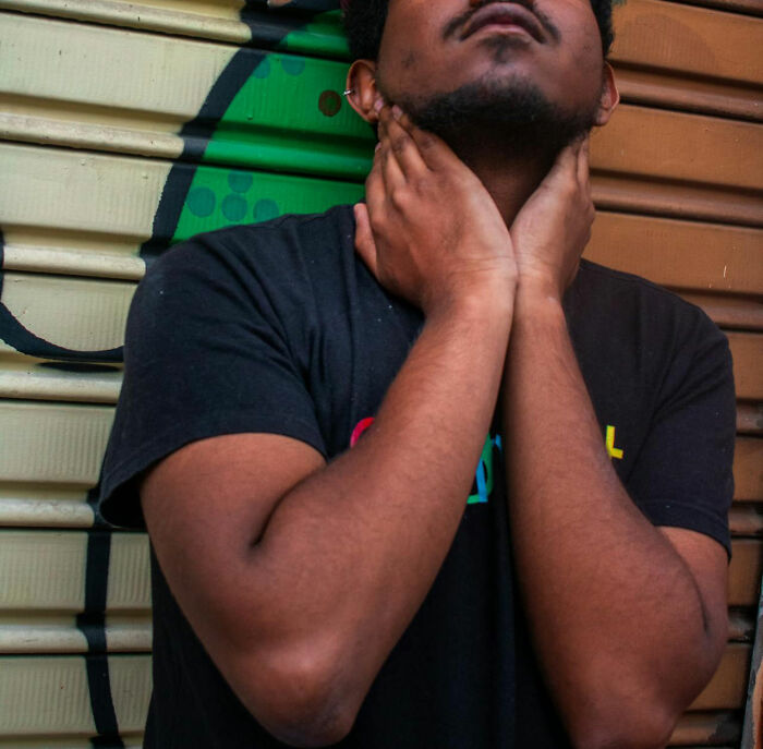 Man holding neck and looking up, showing physical awareness and obvious things in an urban background with graffiti.