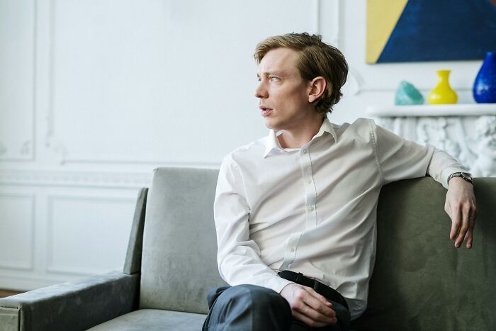 Man in a white shirt sitting on a grey couch, looking to the side, with colorful decor in the background.