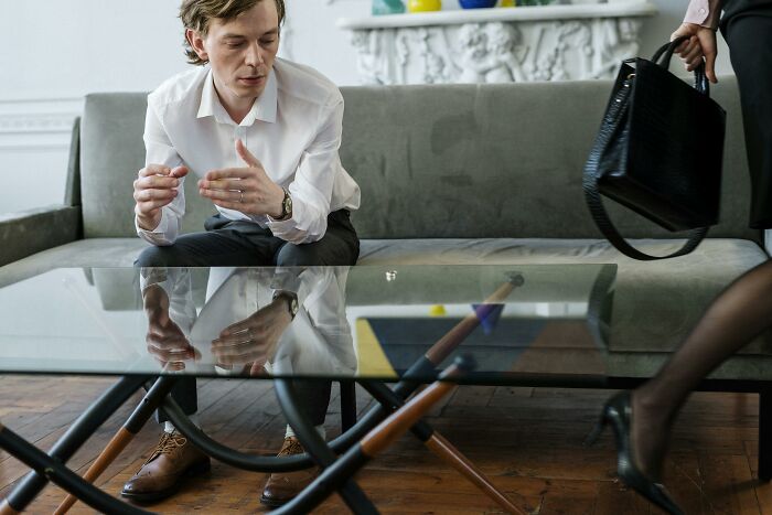 Man in white shirt on sofa, engaged in conversation, highlighting reasons for not attending church.