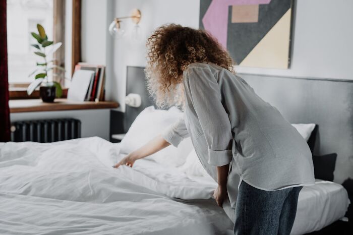Person tidying a bed, demonstrating essential cleaning rules in a bright bedroom setting.