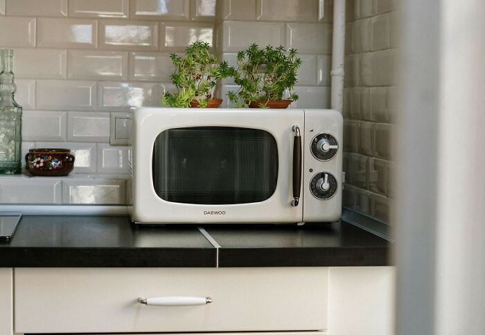 Retro microwave with plants on top in a kitchen, highlighting everyday things that may seem harmless but can be dangerous.