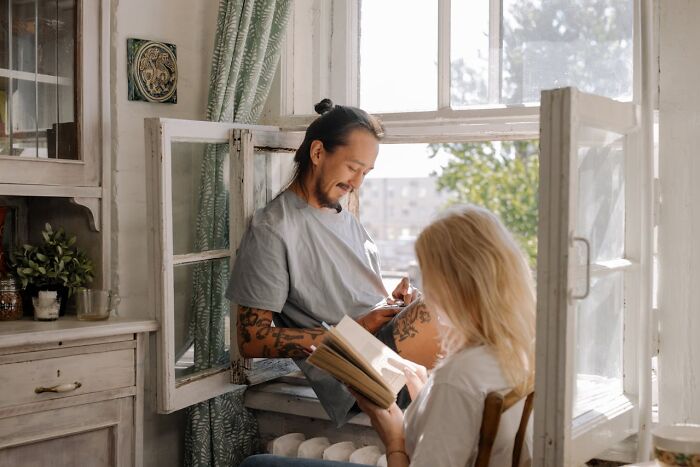A man and woman sitting near an open window, reading and chatting about hygiene tips to stay fresh.