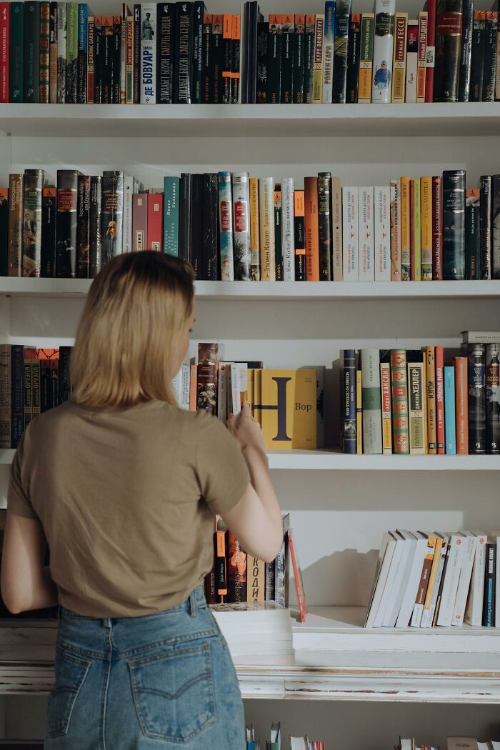 Woman browsing books on shelves in a library setting, illustrating changing consumer choices and restaurant food trends.