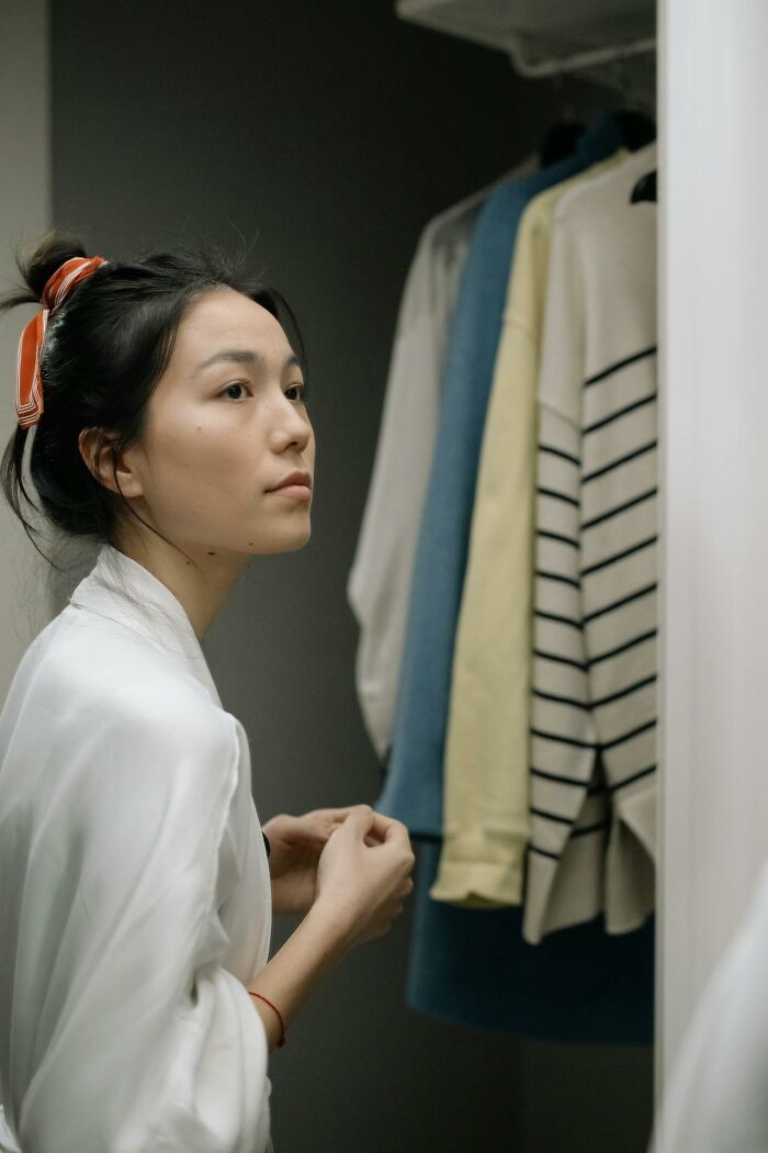 Woman in a white robe looking at clothes in a closet, reflecting common embarrassment topics for women.