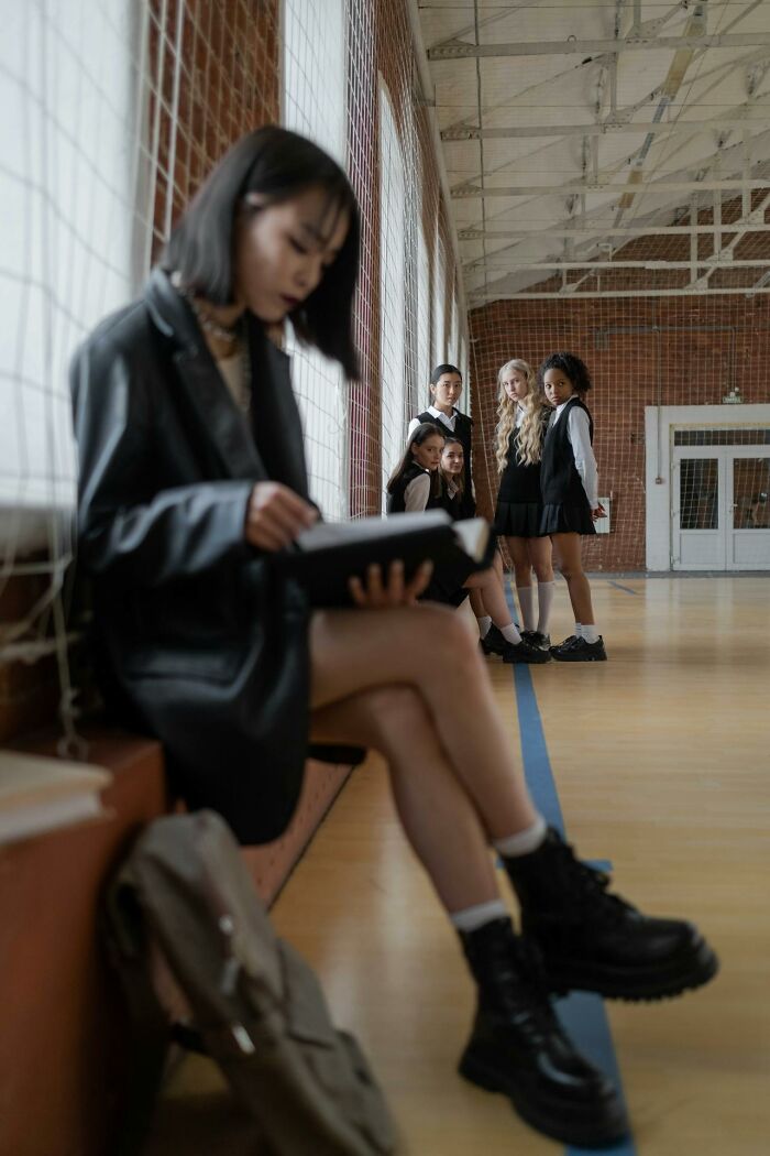 Group of students on the sidelines of a gym with one focused on reading, capturing a scene more traumatizing than realized.