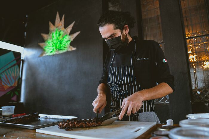Chef in a black apron slicing steak in a stylish kitchen.