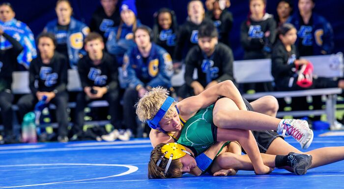 Two young wrestlers compete on a mat, surrounded by a concerned audience.