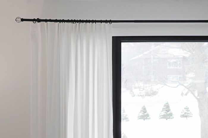 White curtains hanging by a large window with a snowy outdoor view.