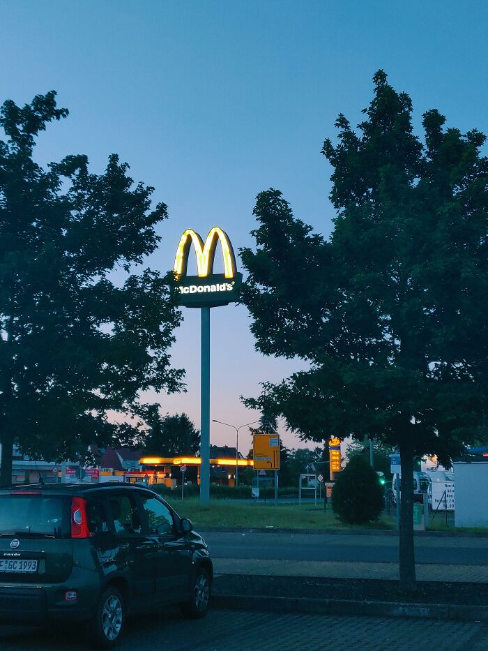 McDonald's sign glowing at dusk near parked car with trees around, illustrating lottery winners' unexpected fortune.