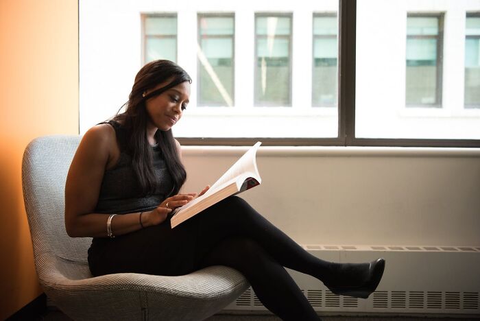Woman peacefully reading a book in a chair by the window, related to mom sanity hacks.