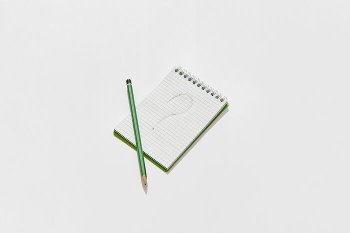 Notepad with question mark sketch and green pencil on white surface, representing plurals challenge and typing test.