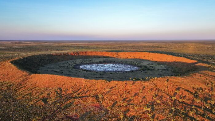 Aerial view of a massive crater landmark in a desert landscape during sunset.