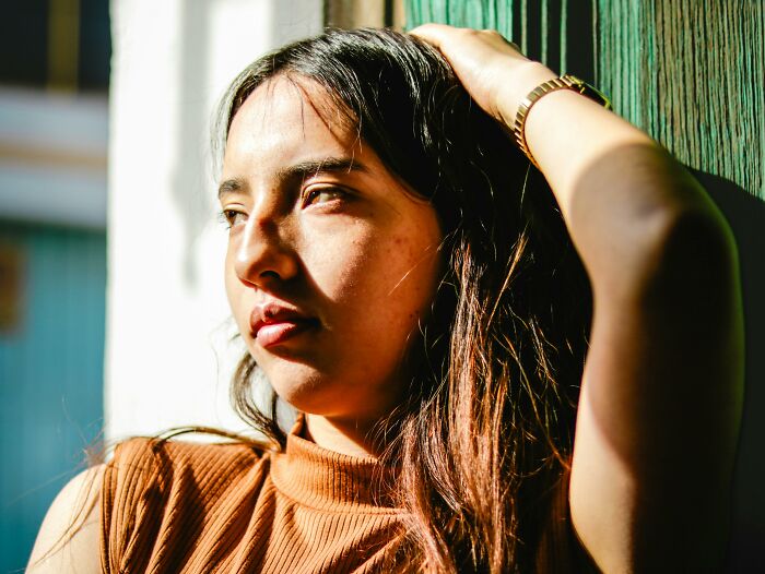 A person in a thoughtful pose, leaning against a wooden surface, with sunlight casting shadows, highlighting a mature look.