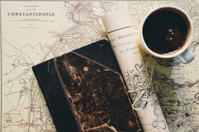 Old maps and a worn book placed next to a coffee cup, symbolizing countries and cities that got a rebrand.
