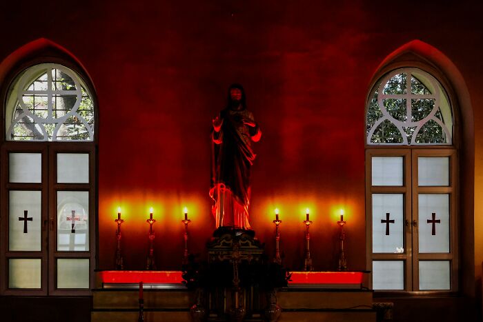 Church interior with candles and a statue, dimly lit, capturing a somber atmosphere.