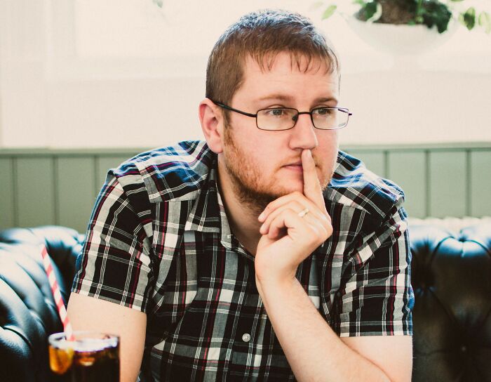 Man in glasses, plaid shirt, pondering in a cafe; relates to viral online thread about stopping church attendance.