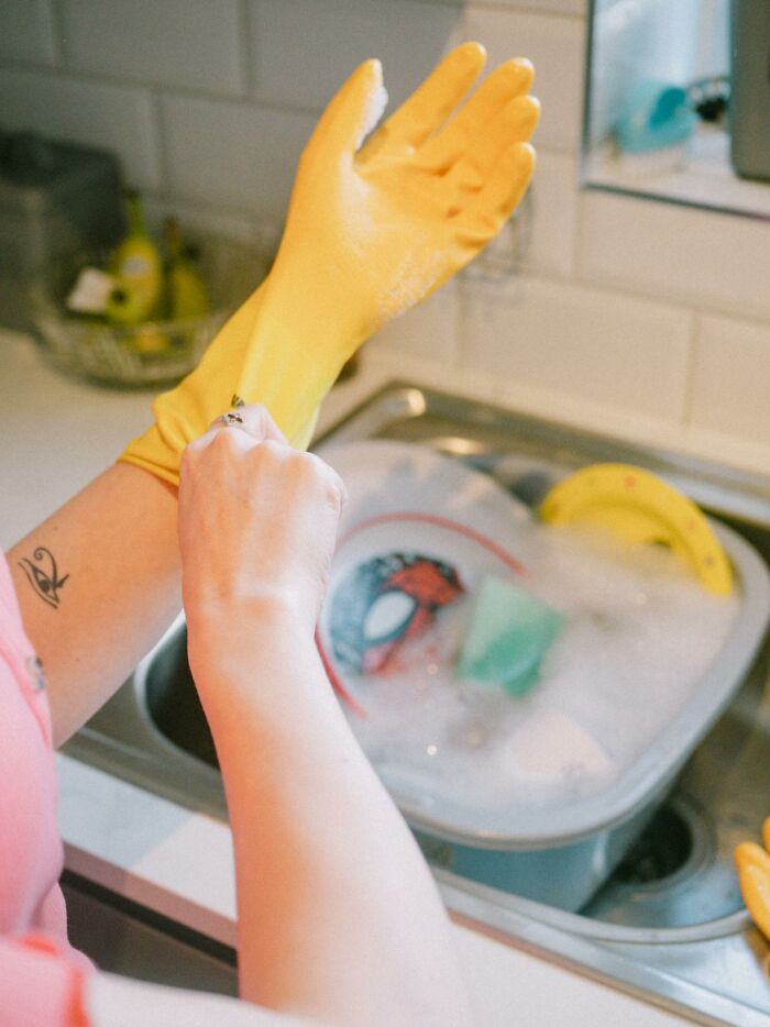 Person putting on rubber gloves for dishwashing, emphasizing cleaning rules with filled sink in background.