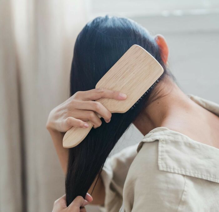 A person brushing long hair with a wooden brush, highlighting fresh hygiene practices.