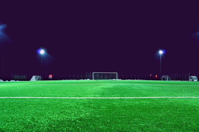 Illuminated soccer field at night with visible goalposts and benches.