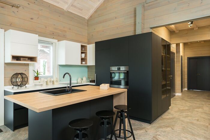 Modern kitchen with island and vessel sink, featuring sleek black cabinets and wooden accents, stylish but not practical.