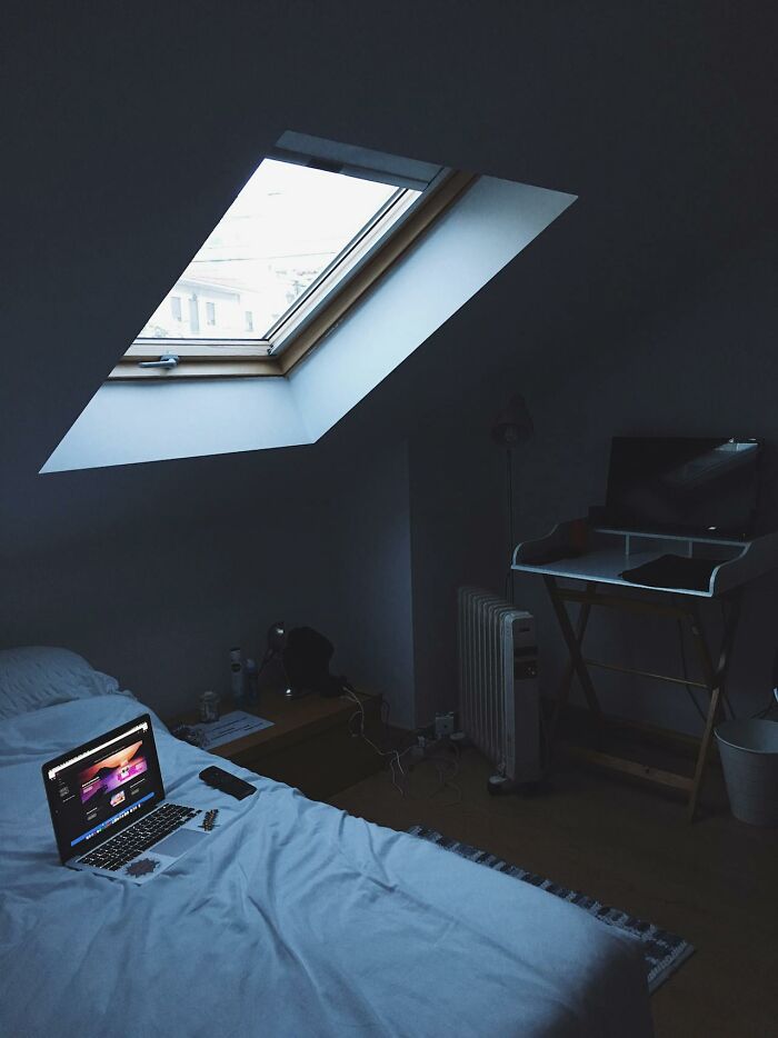 Dimly lit room with a bed, laptop, and desk, showing impractical home setting despite aesthetic appeal.