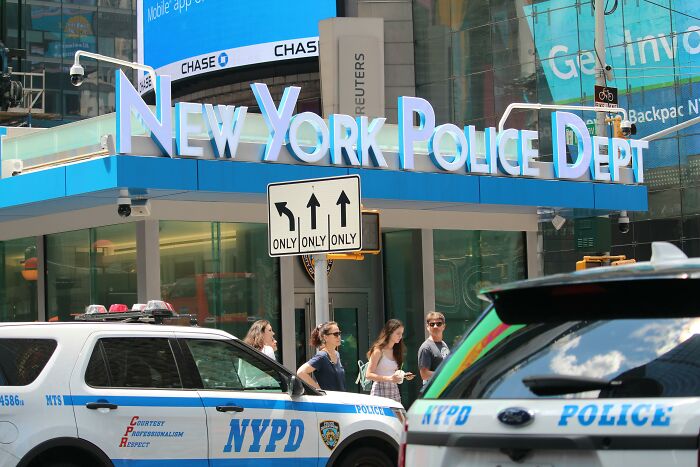 New York Police Department building with signage, NYPD vehicles, and pedestrians in the foreground.