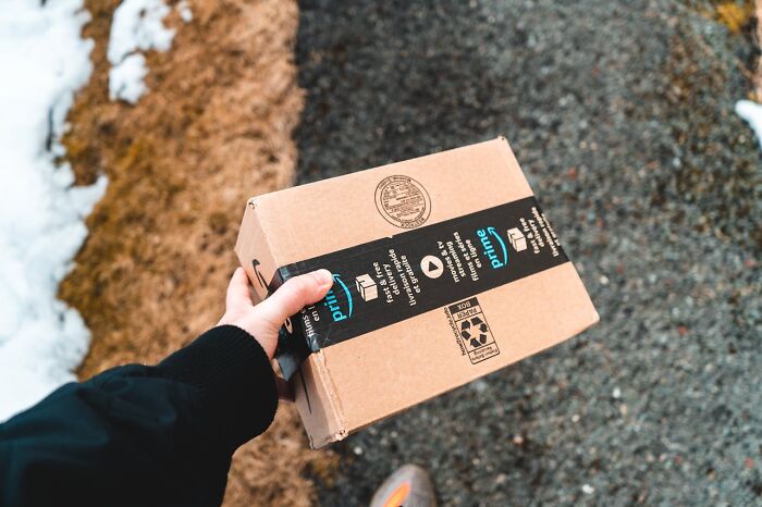 Person holding a cardboard package with Prime tape outdoors on a snowy and gravel path, related to restaurant food delivery.