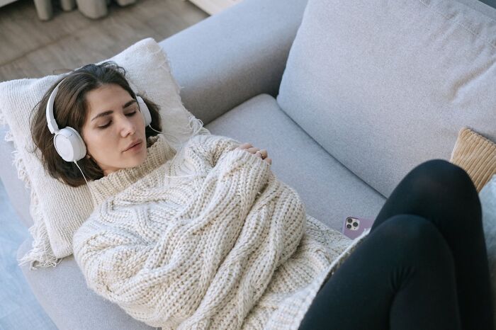 Woman in a cozy sweater wearing headphones, relaxing on a sofa, exemplifying mom sanity hacks.