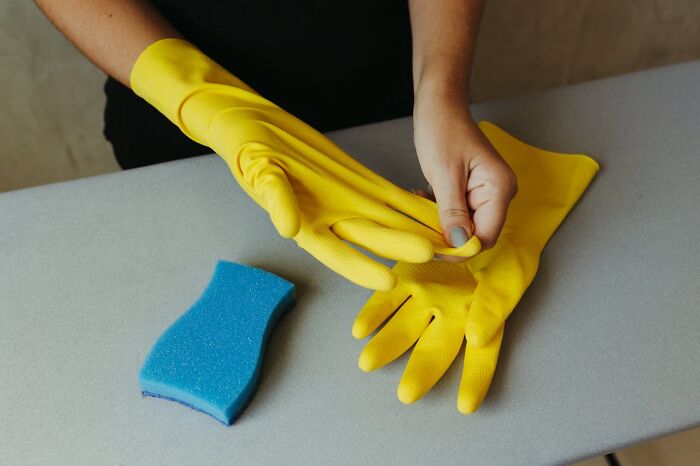 Person putting on yellow gloves near a blue cleaning sponge, symbolizing strict cleaning rules.