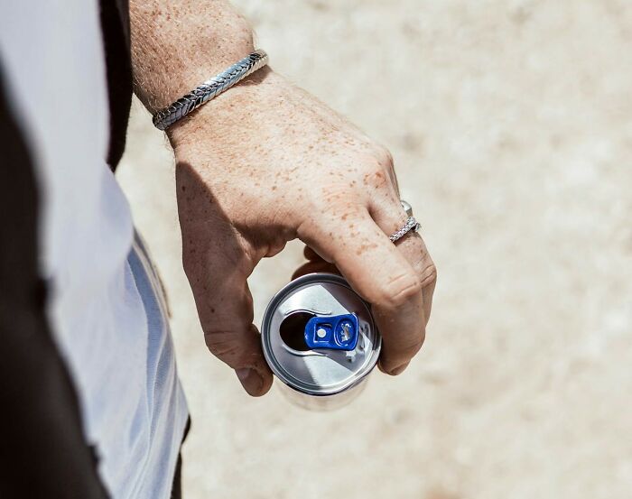 Hand holding a soda can, wearing silver bracelets and rings, illustrating a casual scene with visible freckles on the hand.