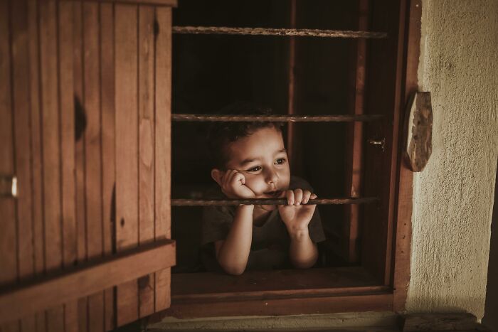 Child looking thoughtfully out a window, hands resting on chin, symbolizing contemplation related to stopping church attendance.