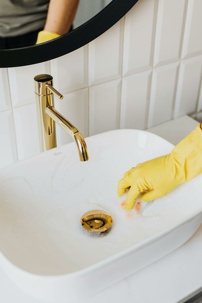 Yellow gloved hand cleaning white sink basin diligently.