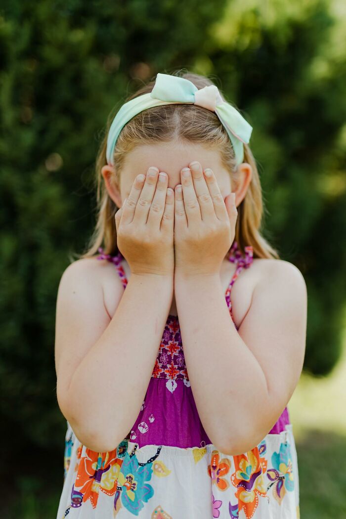 Young girl in colorful dress and bow headband covering her face, representing emotions shared by first responders.