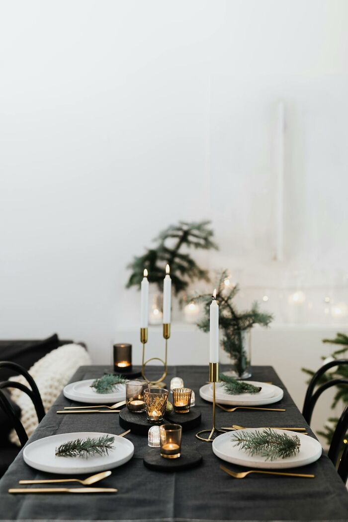 Creepy dining setup with candleholders, evergreen sprigs, black tablecloth, and gold cutlery in a dimly lit room.