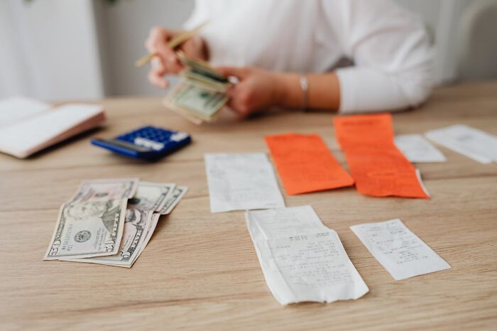 Person counting cash with receipts and calculator on table, illustrating restaurant food price increases and budgeting.