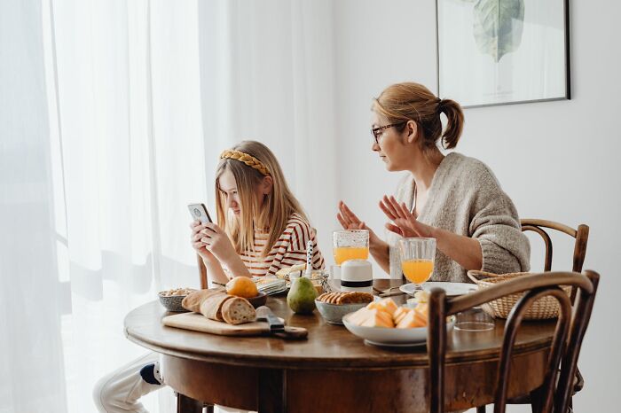 Mom looking frustrated while daughter uses phone, illustrating parenting challenges around the breakfast table.
